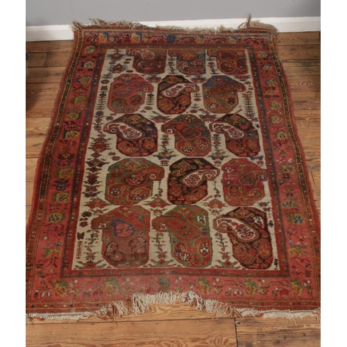 559 - A red ground wool rug featuring floral motifs and fringed edges. Approx. dimensions 180cm x 130cm.