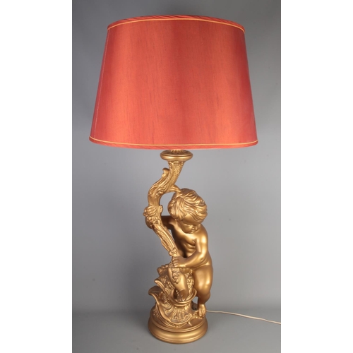 151 - A large gilt lamp formed as a seated putto, with shade. Height to fitting 69cm.