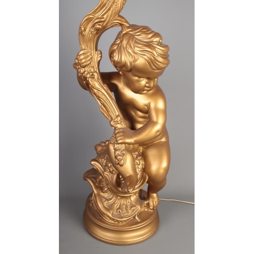 151 - A large gilt lamp formed as a seated putto, with shade. Height to fitting 69cm.