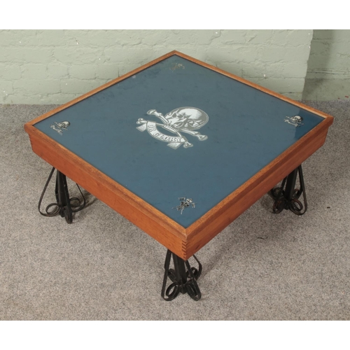 631 - A military style low table, raised on squat ornate supports. Bearing stickers to the top for The Roy... 