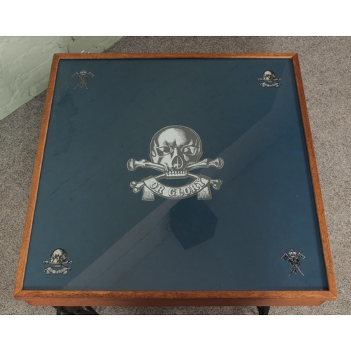 631 - A military style low table, raised on squat ornate supports. Bearing stickers to the top for The Roy... 