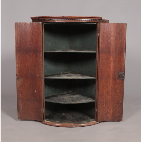 451 - A Georgian oak bow front corner cupboard. Height 99cm.