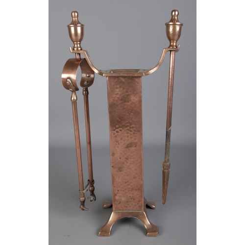 125 - An arts and crafts style copper fireside companion set featuring hammered decoration.