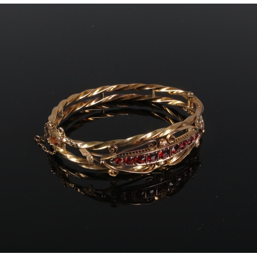 346 - A 9ct Gold bangle, set with a row of nine garnets within a scrolled and rope twist border. Total wei... 