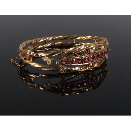 346 - A 9ct Gold bangle, set with a row of nine garnets within a scrolled and rope twist border. Total wei... 