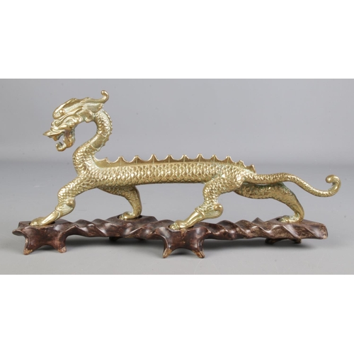 419 - A brass figure of a Chinese dragon raised on hardwood stand. Height 16cm, Length 34cm.