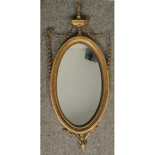 314 - An early Twentieth Century Adam Revival gilt gesso oval mirror, with swag and bow urn style detailin... 