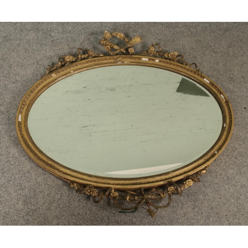 325 - A large gilt framed oval mirror decorated with crossed torches and ribbon swag detail. Approx. dimen... 