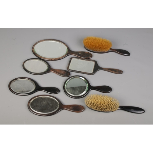 84 - A collection of ebonised dressing table items to include several mirrors and brushes.