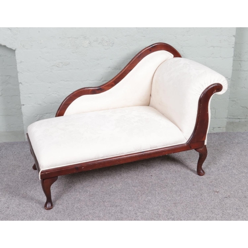 535 - A vintage chaise lounge with a wooden frame and cream upholstery. It features a curved backrest on o... 