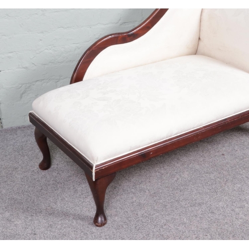 535 - A vintage chaise lounge with a wooden frame and cream upholstery. It features a curved backrest on o... 