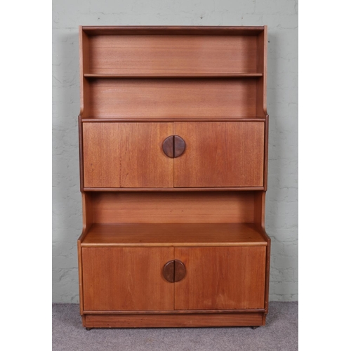 518 - A tall teak unit, raised on casters. Consists of two open bookcase shelves above two sets of cupboar... 