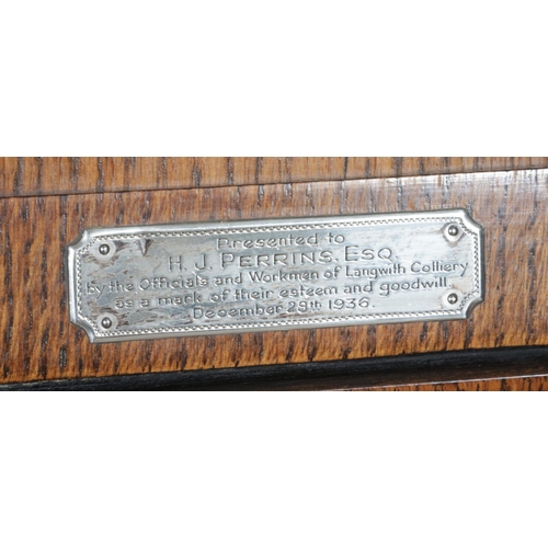 553 - An Art Deco style oak long cased clock with Arabic numeral markers and presentation plaque 'Presente... 