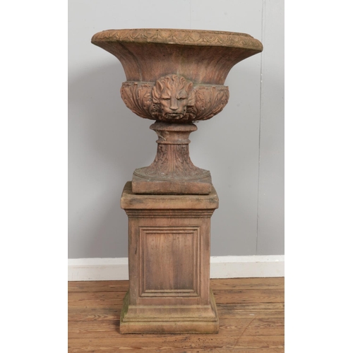 135 - A pair of antique terracotta garden urn planters, raised on plinths. The planters having twin lion m... 