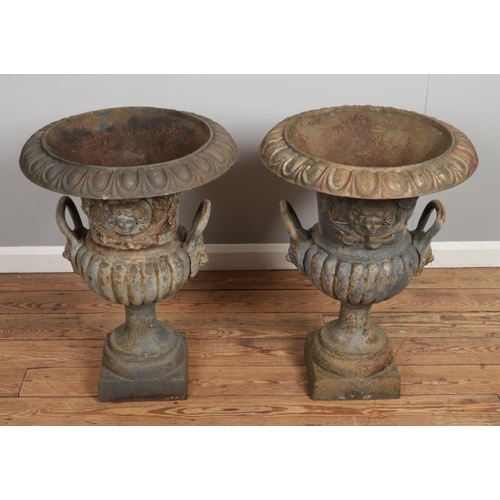 136 - A pair of Victorian cast iron garden urns. Having mask decoration and twin lion mask handles. Height... 