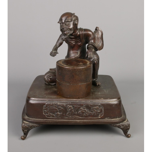 14 - A Japanese bronze desk stand formed as a seated man and a barrel raised on square plinth with scroll... 