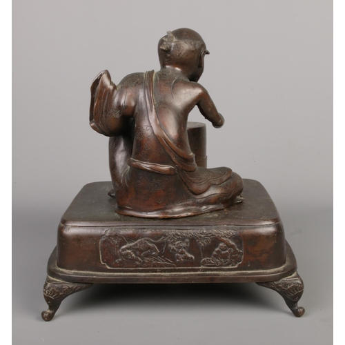 14 - A Japanese bronze desk stand formed as a seated man and a barrel raised on square plinth with scroll... 