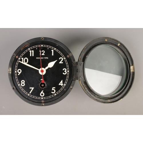 30 - A British Royal Navy mechanical bulkhead clock with black dial and broad arrow mark. Numbered 0552/4... 