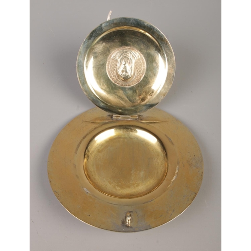 76 - A German silver gilt religious dish with hinged cover. The front of the cover embossed with a image ... 