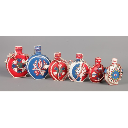 214 - A set of six vintage Folk Art leather-covered flasks, featuring rustic, colourful leather with flora... 