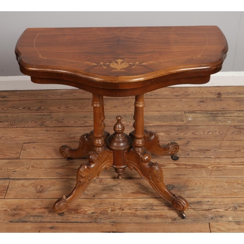 527 - A walnut inlaid fold over card table raised on four turned supports and scroll carved legs. Approx. ... 