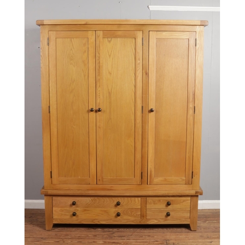 535 - An oak wardrobe. With three panelled doors and drawer base. Height 191cm, Width 148cm, Depth 56.5cm.