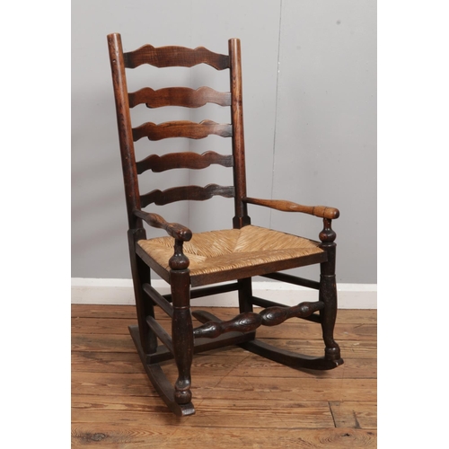 540 - A Nineteenth Century ash/elm ladder back rocking chair, with rush seat.