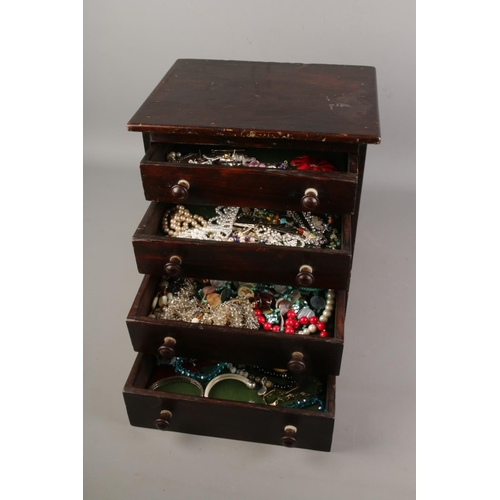 55 - An antique miniature chest of drawers with contents of costume jewellery.