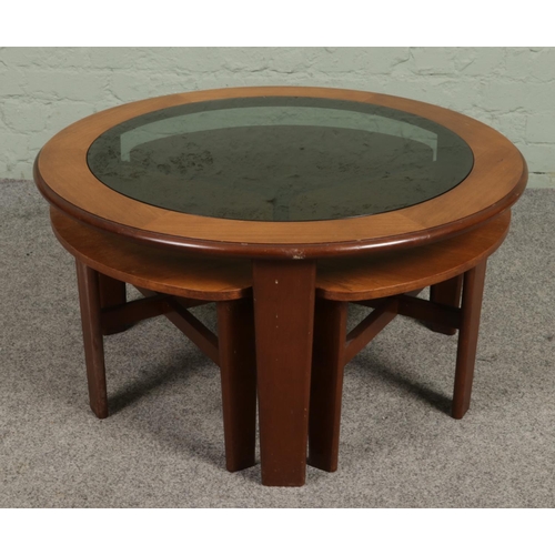 676 - A mid century smoked glass top teak coffee table with three smaller nesting tables. Height 44cm, Dia... 