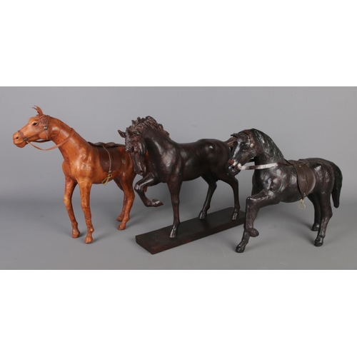 13 - Three horse figure statues, comprising one wooden carved with a base and two vintage leather wrapped... 