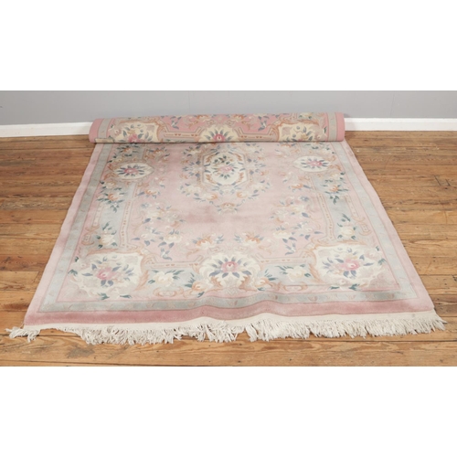 294 - A large pink ground wool rug featuring floral rose design with central medallion and fringed edges. ... 