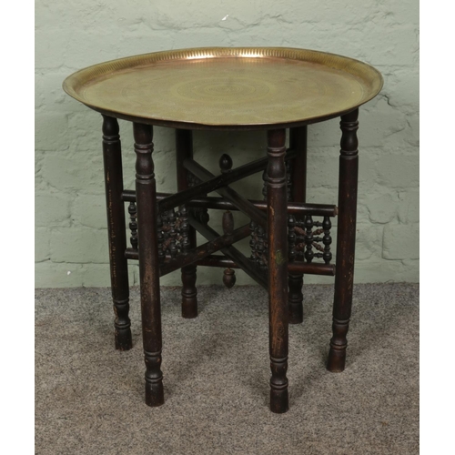 405 - An Indian brass topped table with folding wooden base. Diameter of top: 58cm.