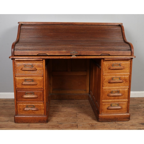 493 - A mid Twentieth Century oak roll top desk, with panelled back, partial fitted interior and two banks... 