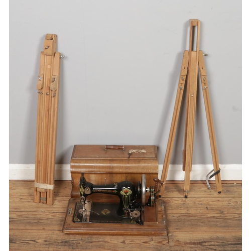 255 - Two artists easels with an antique cased New Portland sewing machine, serial No. 434274 with key.