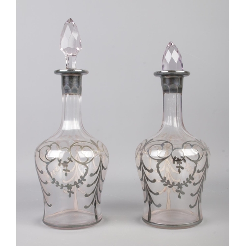 104 - A pair of white metal overlay decanters, featuring swag and bow detailing and cut glass stoppers. He... 