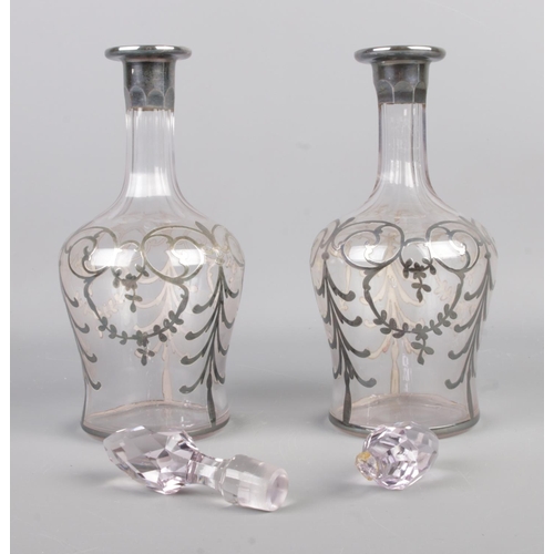 104 - A pair of white metal overlay decanters, featuring swag and bow detailing and cut glass stoppers. He... 