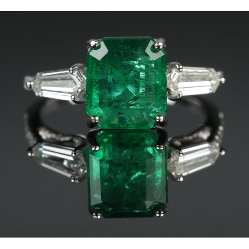 125 - An 18ct white gold emerald and diamond ring. Set with an octagonal cut emerald, flanked by two bague... 