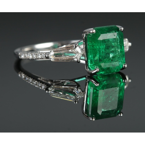 125 - An 18ct white gold emerald and diamond ring. Set with an octagonal cut emerald, flanked by two bague... 