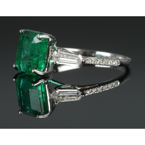 125 - An 18ct white gold emerald and diamond ring. Set with an octagonal cut emerald, flanked by two bague... 