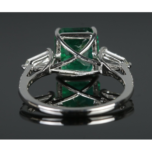 125 - An 18ct white gold emerald and diamond ring. Set with an octagonal cut emerald, flanked by two bague... 