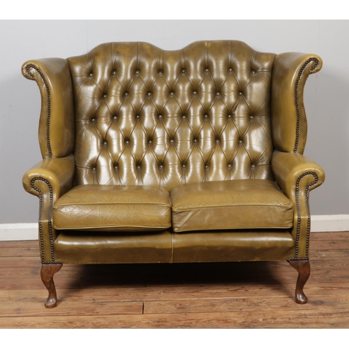 A deep buttoned and studded olive green Chesterfield wingback two-seater sofa. Raised on cabriole supports. Width: 133cm.