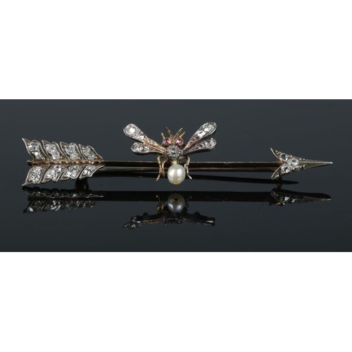 A yellow metal brooch formed as bee perched on an arrow. The bee having diamond set body and wings, pink stones to the eyes and pearl to the tail, with the arrow having diamond set feathers and point. Largest stone approximately ct. Length: 6.7cm. Total weight: 3.7g