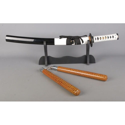 76 - A modern samurai sword in sheath mounted on stand, together with a set of nunchucks. Blade length of... 