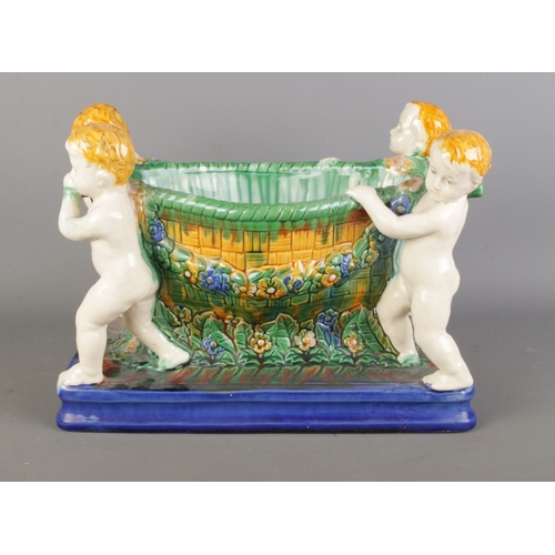 27 - A Majolica ceramic planter/centre bowl featuring four cherubs supporting a detailed floral pattern b... 