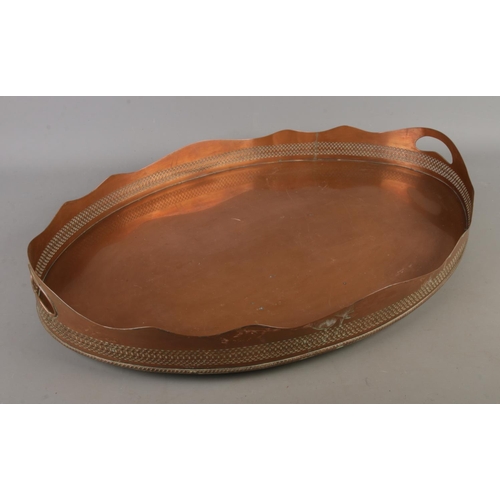 329 - A large twin handled copper serving tray with decorative pierced edge and raised on four small feet.... 