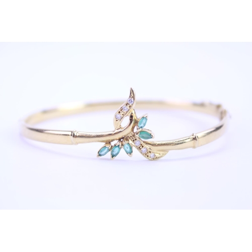 129 - An 18ct Gold ladies bangle in the floral design set with Diamonds & Emeralds. Weight approx 10g.