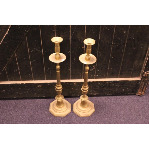 557 - A Large Pair of Turned Brass Altar Candle Sticks resting on Octagonal Bases. Measuring: 68cms high.