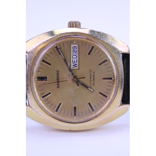 208 - A Garrard Automatic Gold Coloured Wristwatch with day/date, Gold coloured face and black leather str... 