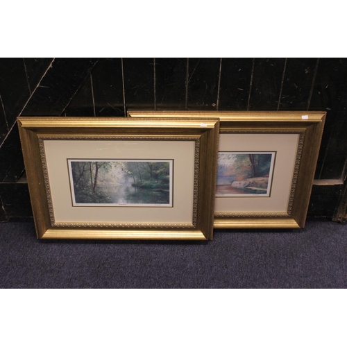 713 - A Pair of gilt framed prints by Ouagbi depicting tranquil waters.