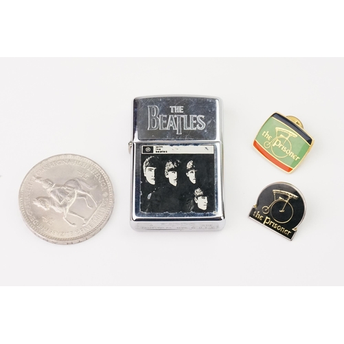 643 - A Zippo Beatles lighter along with a coin and two Prisoner badges.